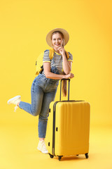 Young woman with suitcase on color background. Travel concept