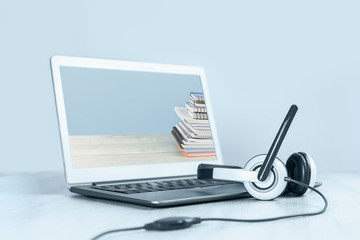 Laptop with pile of notepads on the screen and headphones on white desk blue background. Distant learning or working from home, online courses or school webinar concept.