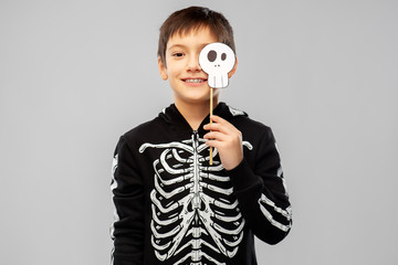 Wall Mural - halloween, holiday and childhood concept - smiling boy in black costume of skeleton with scull party prop over grey background