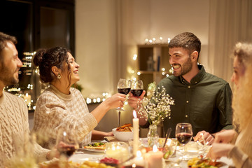 Wall Mural - holidays, celebration and people concept - happy friends having christmas dinner at home drinking non-alcoholic red wine