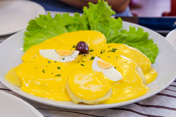 Papas a la Huancaína is a delicious Peruvian dish consists in sliced cooked potato with an aji and fresh cheese yellow sauce, boiled eggs and olives. Traditional Peruvian food concept.