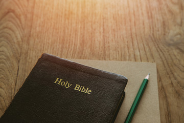 Holy bible with note book and pencil on wooden table, copy space