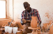 Focused African Guy Working In Pottery Workshop, Painting Ceramic Jug He Created