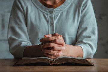 Wall Mural - Woman praying, hands clasped together on her Bible. copy space.