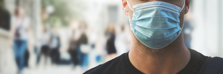 man wearing medical face mask at crowded city street during virus pandemic. banner copy space