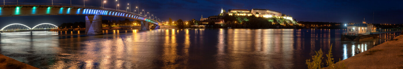 Wall Mural - Petrovaradin fortress in Novi Sad, Serbia and Rainbow bridge illuminated with colorful street lights and reflection in the Danube river water, panorama shot