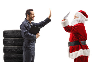 Poster - Auto mechanic with a pile of tires gesturing high five with Santa Claus