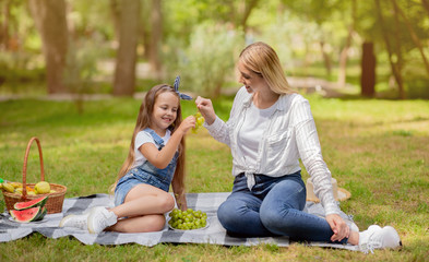 Mother And Daughter Eating Grapes Sitting On Plaid In Park