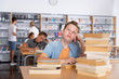 © JackF - Upset schoolboy sitting with stacks of books in library indoor..