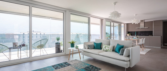 Modern living room with designer furniture. Sofa with light cushions and balcony view. Behind the modern kitchen with island.