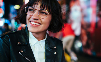 Carefree hipster tourist in optical spectacles for provide eyes protection enjoying evening walk in New York, cheerful Caucasian woman dressed in trendy leather jacket laughing on Manhattan