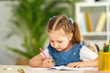 © skif - little girl is sitting at a table and writing in a notebook. learning concepts