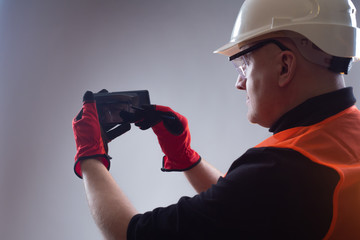 A man in a white hard hat is holding a smartphone. Builder with a smartphone in his hands. The engineer coordinates the project details with the customer.