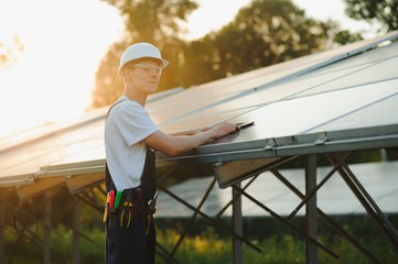 The portrait of a young engineer checks with tablet operation with sun, cleanliness on field of photovoltaic solar panels. Concept: renewable energy, technology, electricity, service, green power.