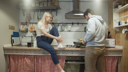 Young husband cooks something on pan and his wife laugh to him