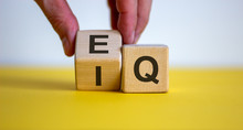 Hand Flips A Cube And Changes The Expression 'IQ' To 'EQ'. Beautiful Yellow Table, White Background. Concept Of Emotional And  Intelligence Quotient. Copy Space.