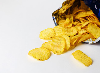 one of the types of snacks, fast food, junk food - ruffled potato chips spilling out of an open bag on a white background