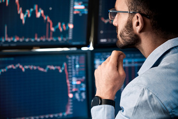 Stock Traiding. Trader sitting at office monitoring market analyzing candle bar price flow on monitors concerned close-up