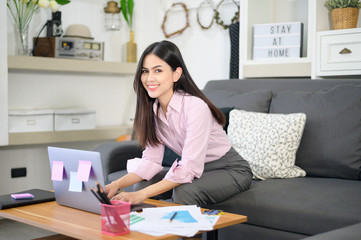 A business woman is working with laptop computer and analyzing business growth graph data in living room, Work from home , business technology concept .