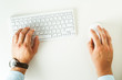 © alexanderon - Man is holding his hands on the white computer keyboard and mouse. Flat lay of the white minimalists working place