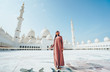A young girl in hijab stands against the background of the abu dhabi mosque.