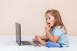© Юлия Немченко - A little girl in blue clothes is sitting on the bed, typing and playing on a laptop. Concept for kids internet safety, social networking or education and homework