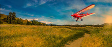 Vintage Bi-plane Flying Over Golden Harvest Fields At Dawn Landscape.
