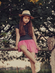 Wall Mural - Fashion kid girl sitting in green park and posing in yellow straw hat and bright pink skirt, yellow shoes. Closeup nature summer style portrait. Vintage