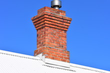Vintage Red Brick Chimney With Modern Metal Lining On Top Of White Corrugated Sheet Metal Roof.
