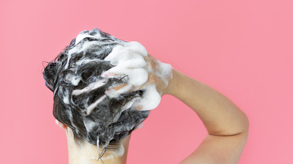 A girl washes her hair with shampoo on pink background, rear view copy space