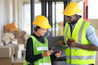 © Akarawut - African American and Asian workers wearing safety vest while working in warehouse checking for the inventory using digital tablet