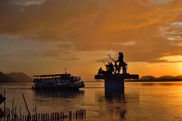 Silhouette of Lachit Borphukan statue during sunset with a ship passing in background in river brahmaputra.	