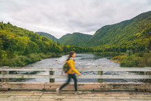Hiker Woman With Backpack Walking On Bridge Crossing River. Motion Blur Of Tourist Hiking In Outdoor Nature Fall. Autumn Traveling Hike In Quebec, Canada.