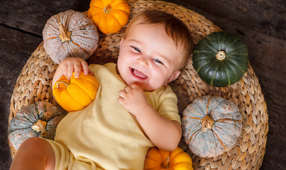 happy cute baby on the basket with different pumpkins