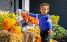 African-American Toddler Playing With Halloween Decorations In Front Yard Of His House In Midwest While Looking At Camera