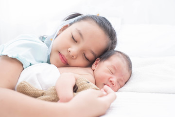 Poster - little sister hugging her newborn brother. toddler kid meeting new sibling. love, trust and tenderness. cute girl and new born baby boy relax in a white bedroom. family with children at home.