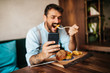 © hedgehog94 - Handsome middle age man sitting in restaurant and enjoying in delicious burger. He is happy and smiled and uses his smart phone to talk with someone.