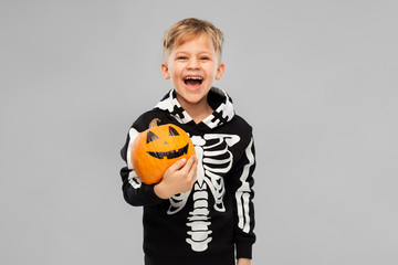 halloween, holiday and childhood concept - happy laughing boy in black costume with skeleton bones holding jack-o-lantern pumpkin over grey background