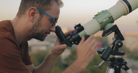 Wall Mural - astronomer with a telescope watching at the stars and moon with blurred city background.