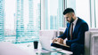 © BullRun - Concentrated office worker using laptop and writing notes at office