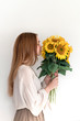 Beautiful young woman in linen dress holding sunflowers bouquet on white background. Autumn concept.