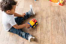 Overhead View Of African American Boy In Jeans Playing With Toy Truck On Wooden Floor
