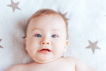 Wall Mural - Photo of a frightened baby, a newborn baby with blue eyes and blond hair lying on a light blanket with brown stars