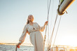 © Artem Varnitsin - Portrait of mature woman in dress standing on yacht at sunset. Beautiful senior woman holding a rope and looking away.