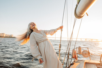 Canvas Print - Happy senior woman wearing dress holding a rope on yacht