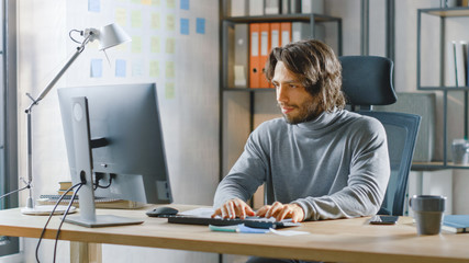 Poster - Handsome Long Haired Entrepreneur Sitting at His Desk in the Office Works on Desktop Computer, Working with Documents, Charts, Graphs, Statistic and Strategy. Creative Entrepreneur Using Computer