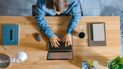 Aufkleber - Top View Shot: In the Office Businessman Sitting at the Wooden Desk Works on a Laptop in his Home Office. He Types, Writes Emails, Surfs the Internet, Designs Software