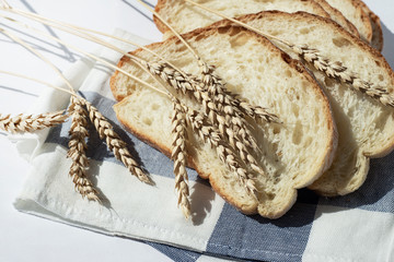  Several pieces of wheat bread on a kitchen napkin with ears of wheat. Homemade ciabatta. Copy space for text.