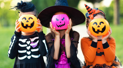 Happy Halloween! funny children in carnival costumes hide their heads behind buckets   pumpkins outdoors.