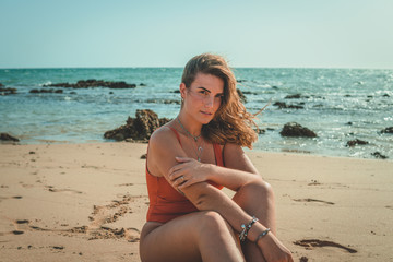 Beautiful young European woman with an orange swimsuit sitting on a beach in Cádiz